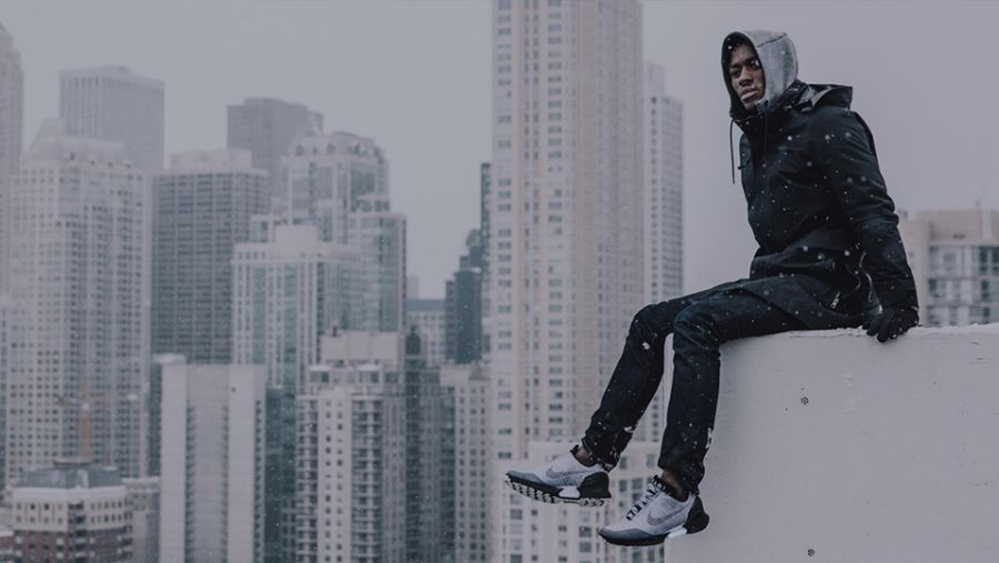 Man sitting on ledge of building wearing Nike Hyper Adapt sneakers. City skyscrapers in background
