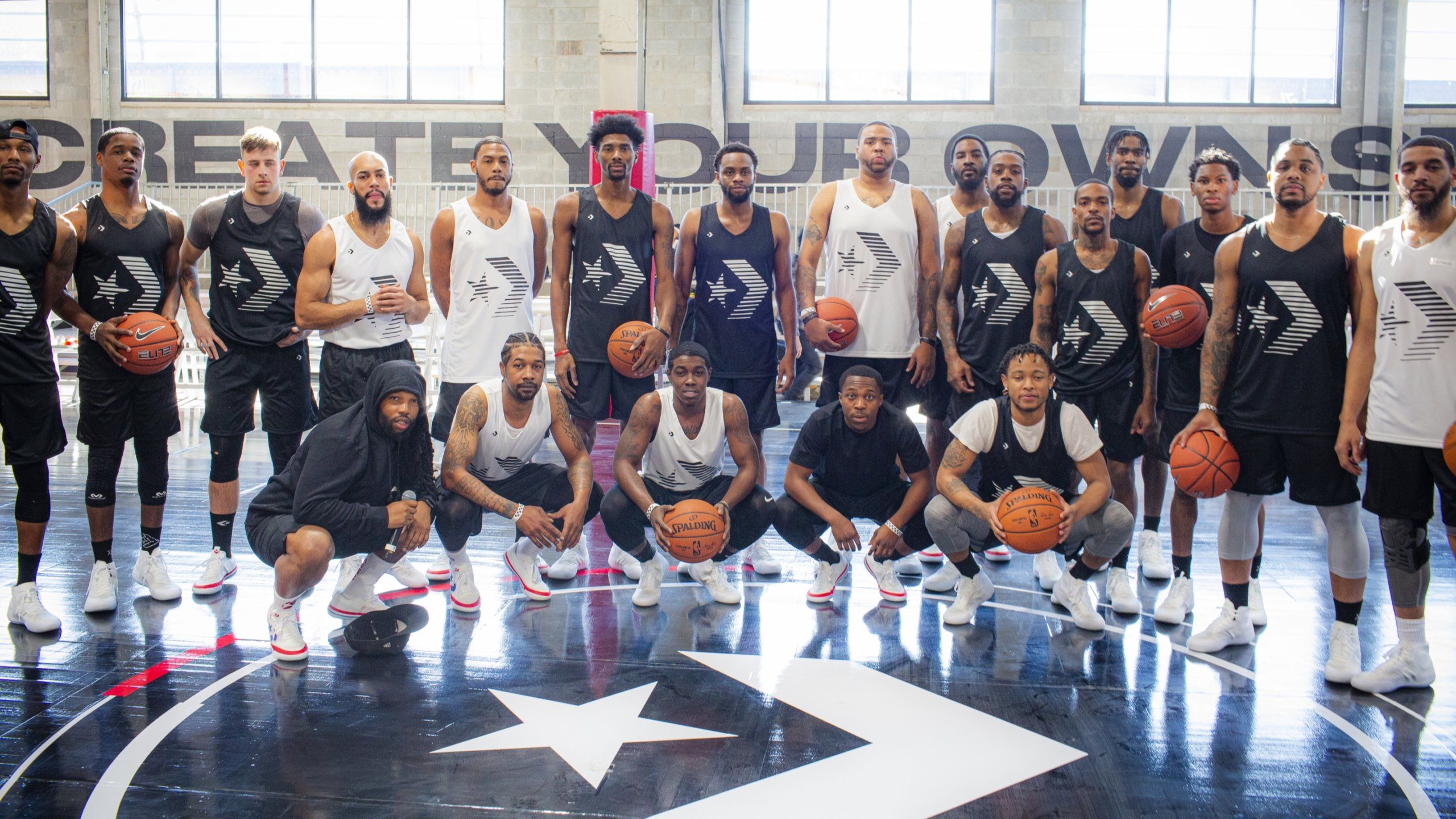 Twenty basketball players posing on court. All players wearing Converse jerseys. court has large Converse star logo.