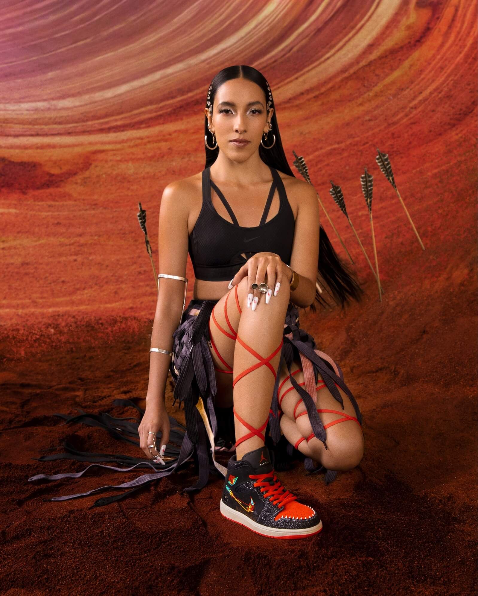 Woman kneeling wearing Nike Día de muertos sneakers with illustrated background including arrows embedded into ground
