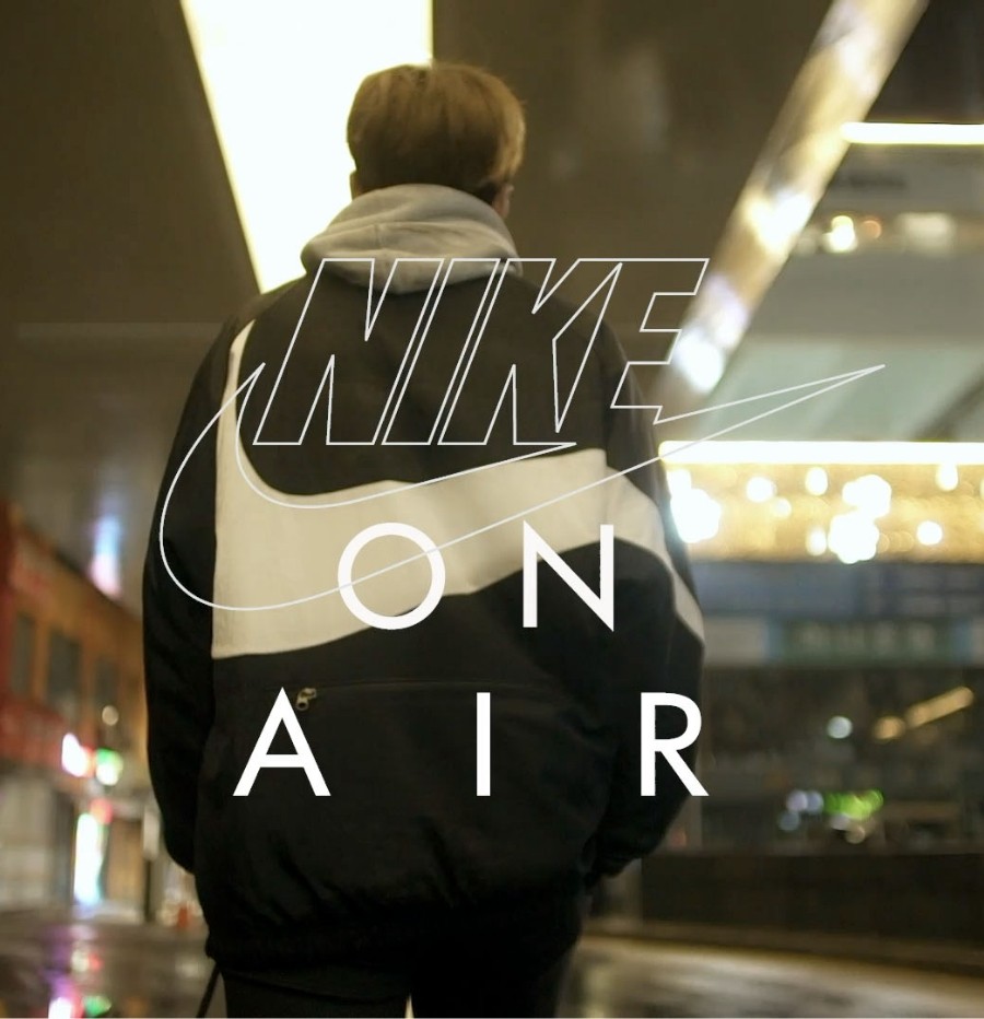 Back View of man walking in Nike jacket with very large swoosh on the back. Nike ON AIR text overlayed