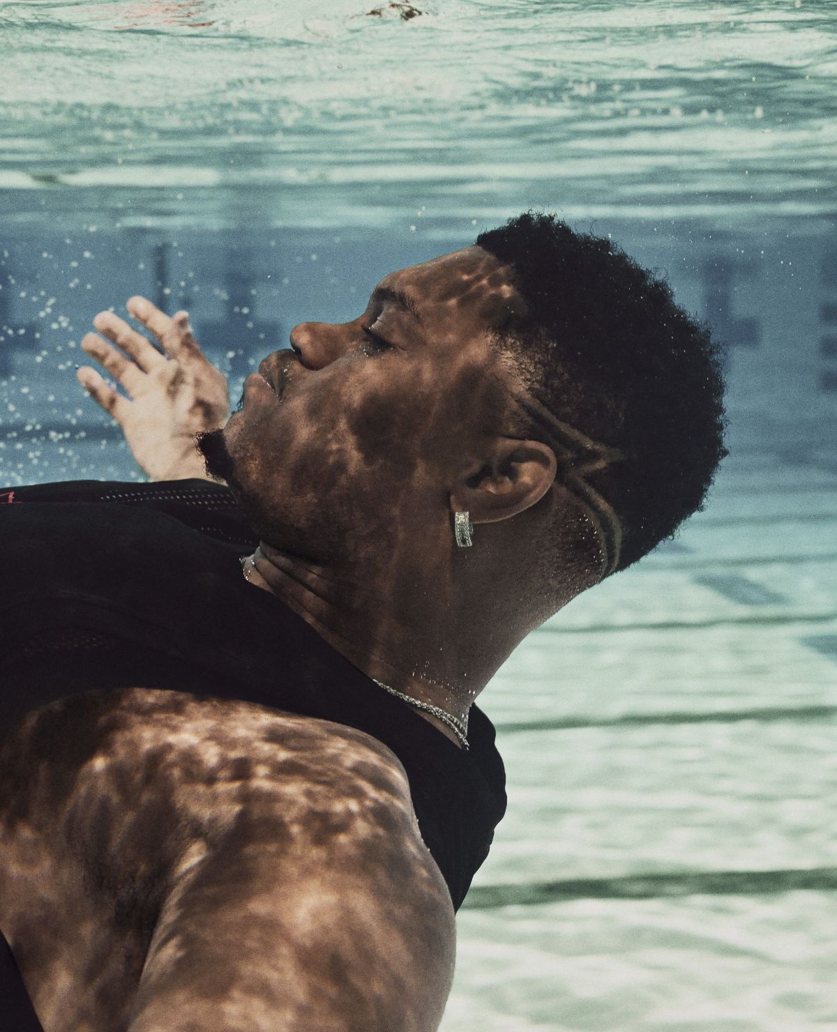 Zion's face and arms outstretched face up, underwater in a pool