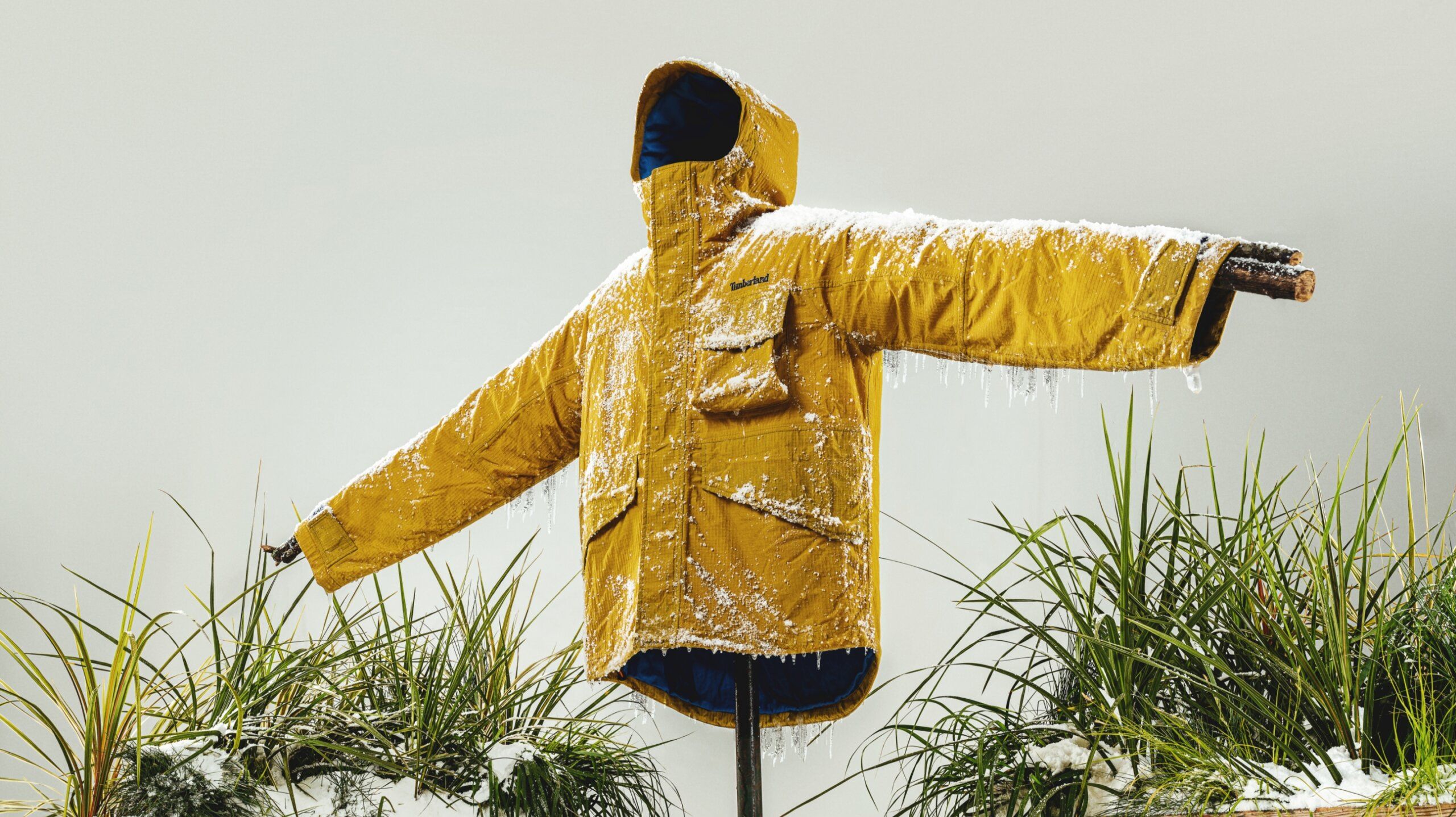 Timberland jacket with snow and icicles. Jacket is propped up with sticks like a scarecrow