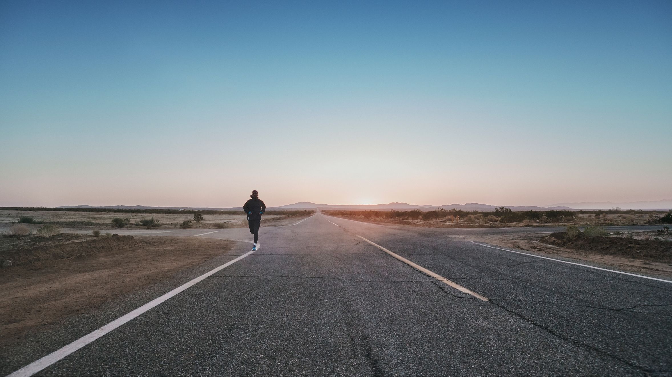 Man running in distance on flat stretch of empty road at dusk