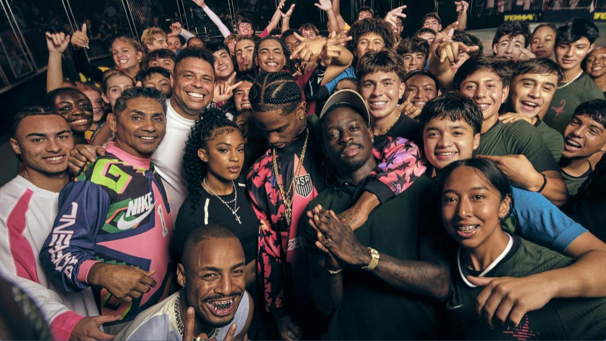 A large group of people, mainly teenagers, pose closely together and smile for a group photo; some wear sport jerseys and casual clothing.