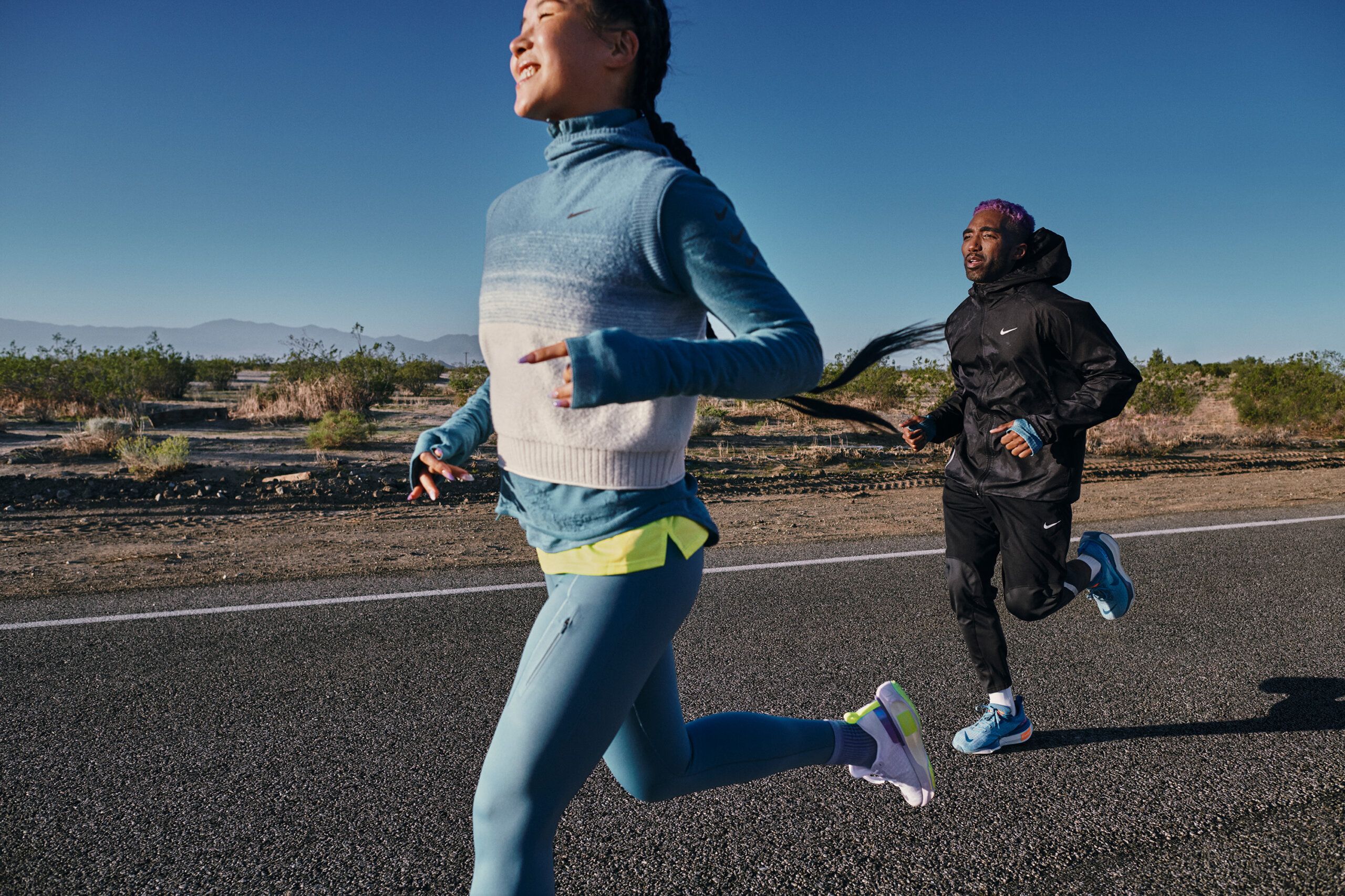 Mi Jang and Chris running together on empty flat road with desert scenery and blue sky background