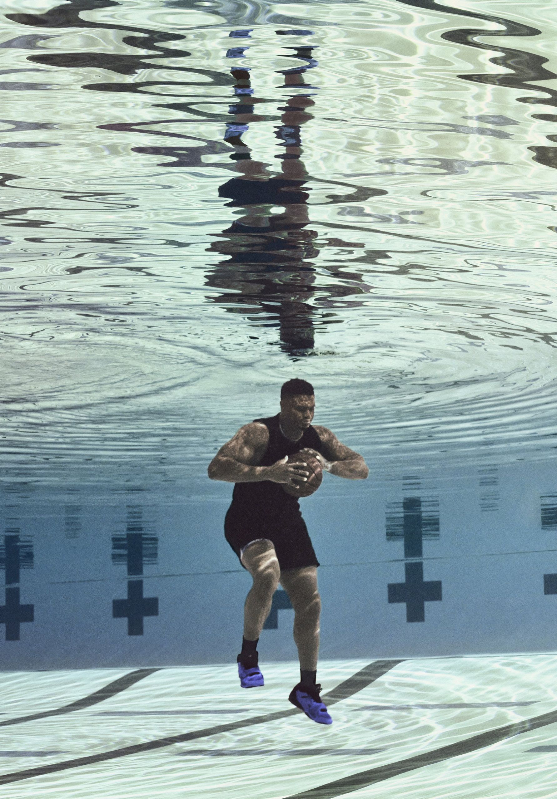 Zion Williamson underwater in swimming pool. There is a mirror like reflection on surface of water with ripples