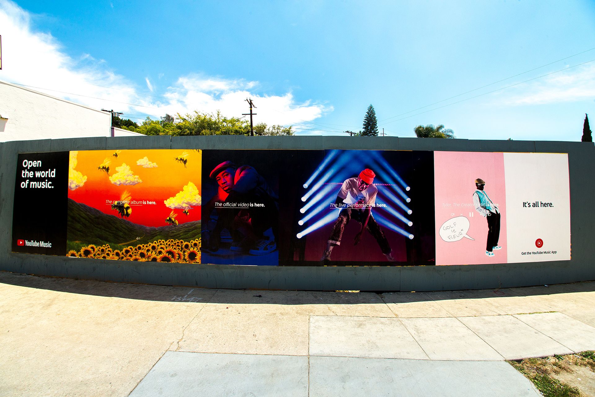 Various YouTube Music poster ads displayed on green wall next to sidewalk.