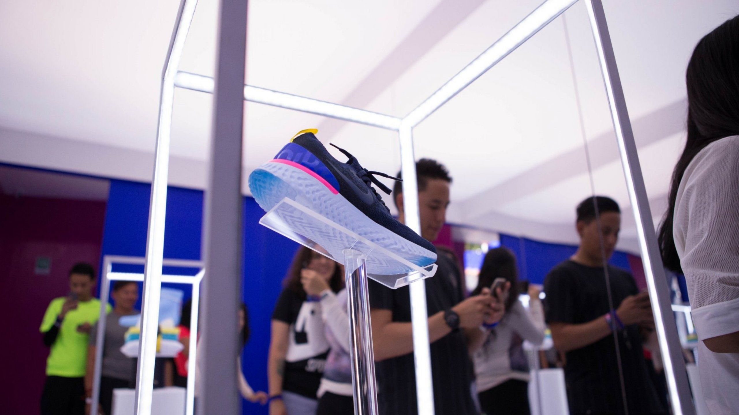 Nike React shoe on display in exhibit. Young people on their cell phones in background