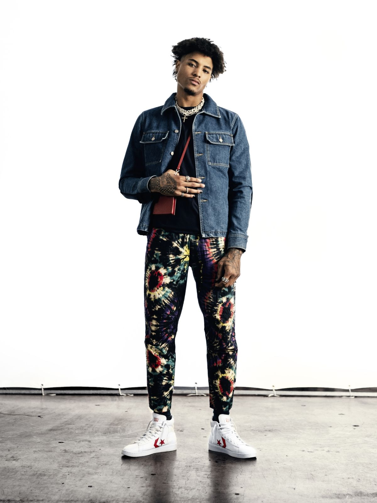 Kelly Oubre Jr standing wearing denim jacket, tie dyed pants and Converse Pro Leather high top sneakers