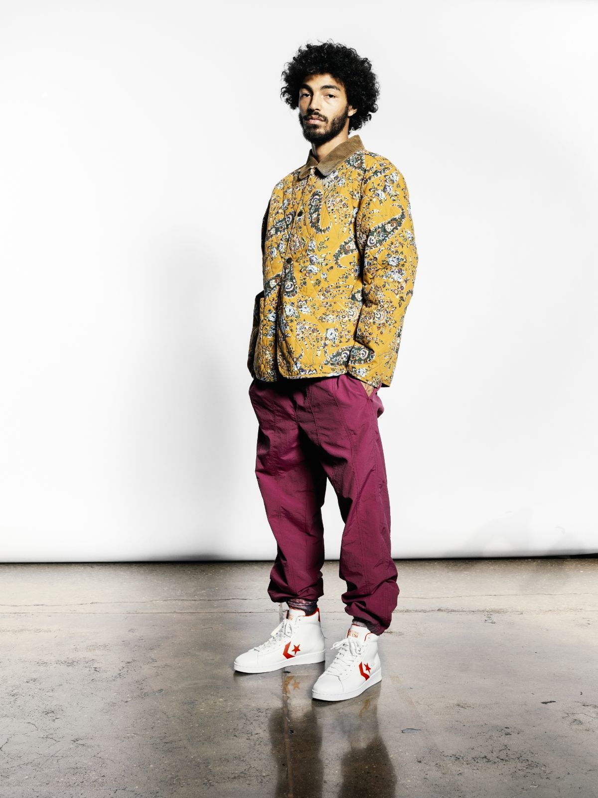Sage Elsesser standing in floral shirt, red pants and white and red converse pro leather high top sneakers