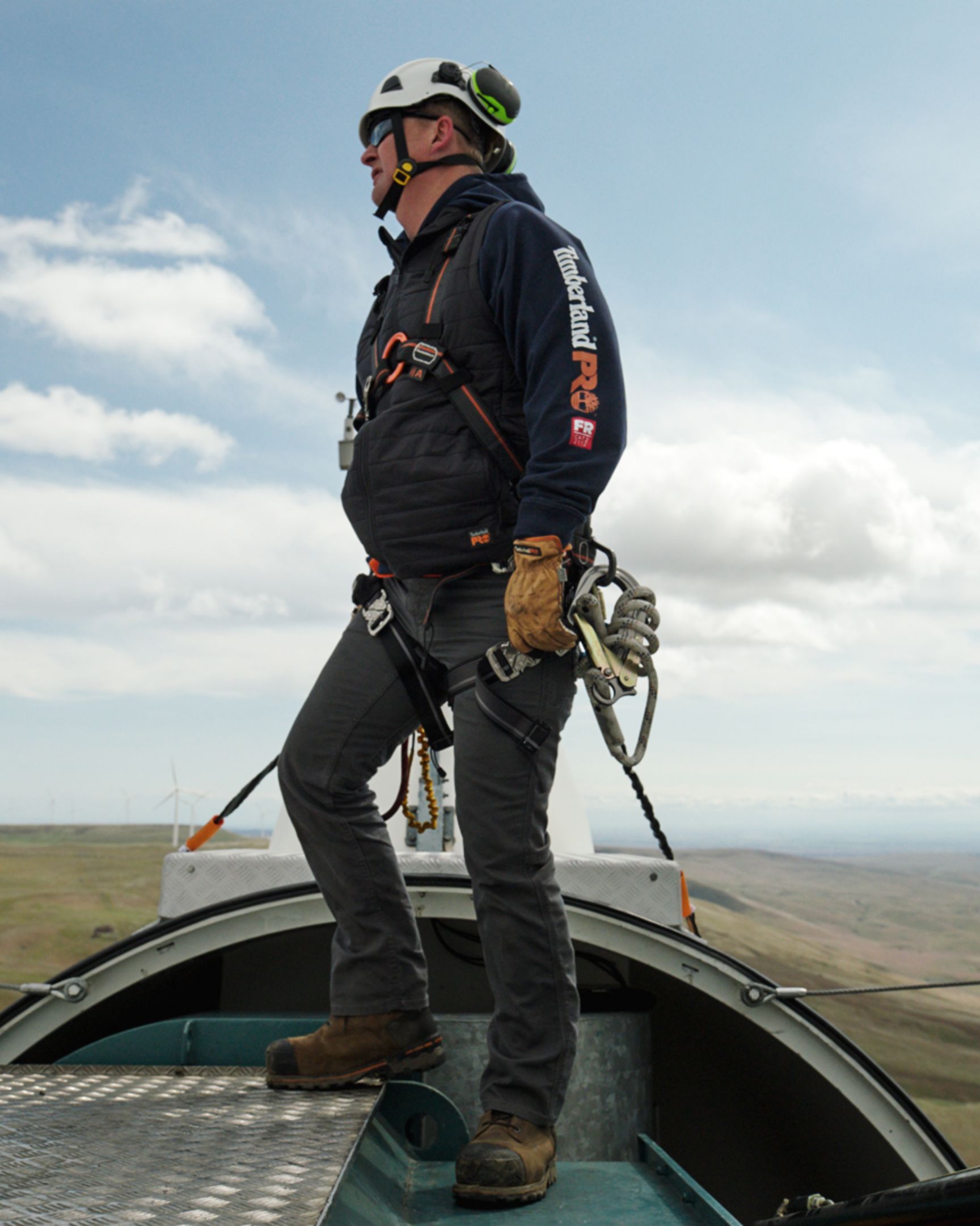 Man strapped into top of power-generating wind mill wearing a timberland pro sweatshirt and Timberland Boondock workboot
