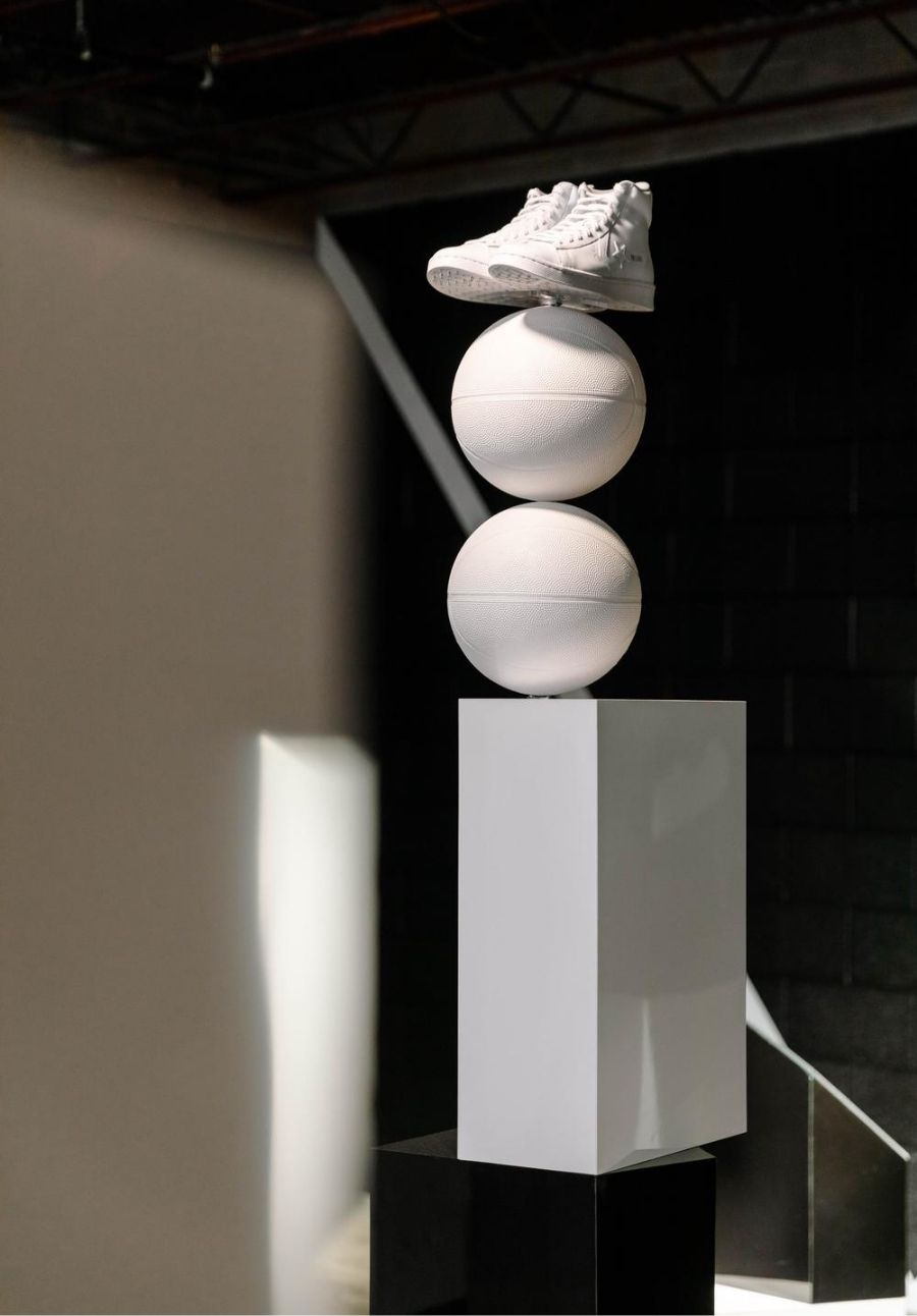 Sculpture of white rectangle base, 2 basketballs painted white and stacked, and pair of Converse All Stars all white at top
