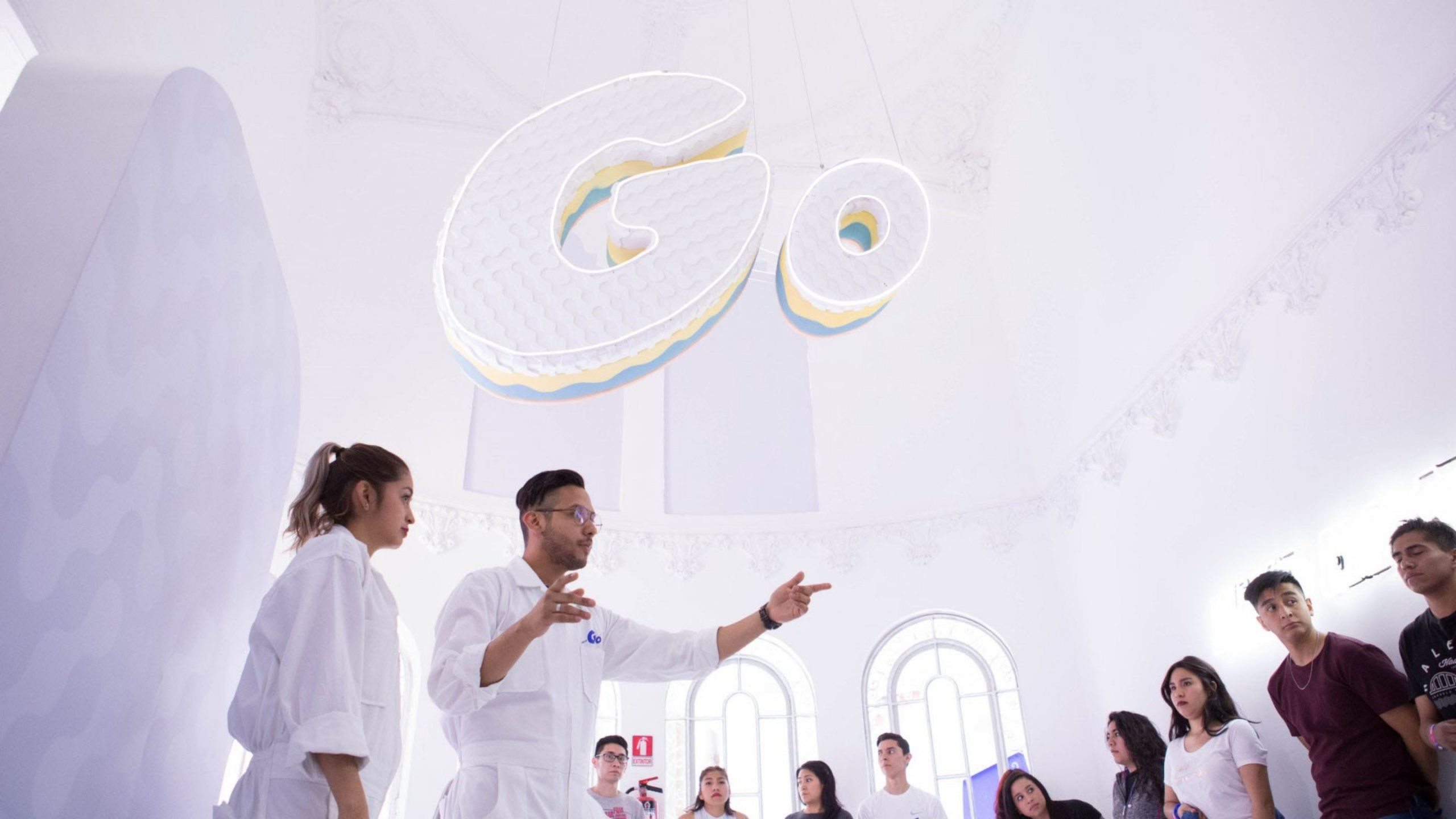 Two people in white jumpsuits with Go logo lead a tour of the House of Go to a group of young people