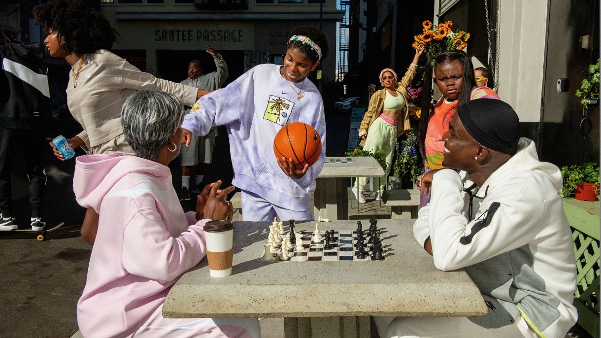 People playing chess talking to woman with basketball in a busy downtown public space