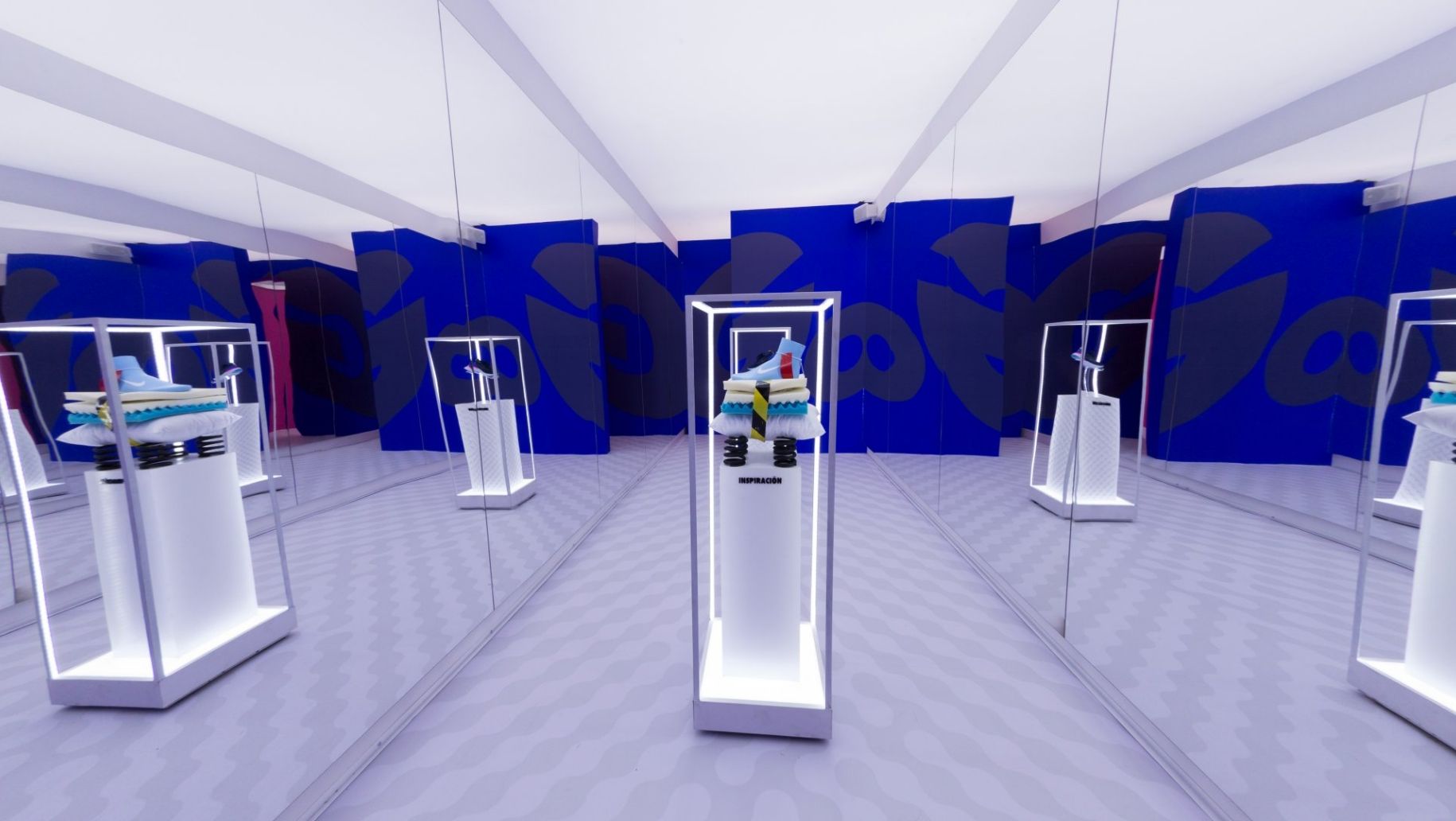 Mirrored room exhibit showing inspiration of shoe with multiple layers of foam and 3 large springs as sole in one podium and actual Nike React sneaker in another podium.