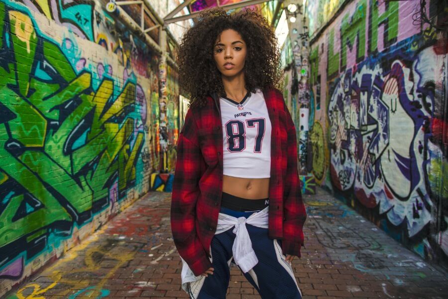 Women in graffiti painted alley wearing flannel shirt and number 87 Patriots top