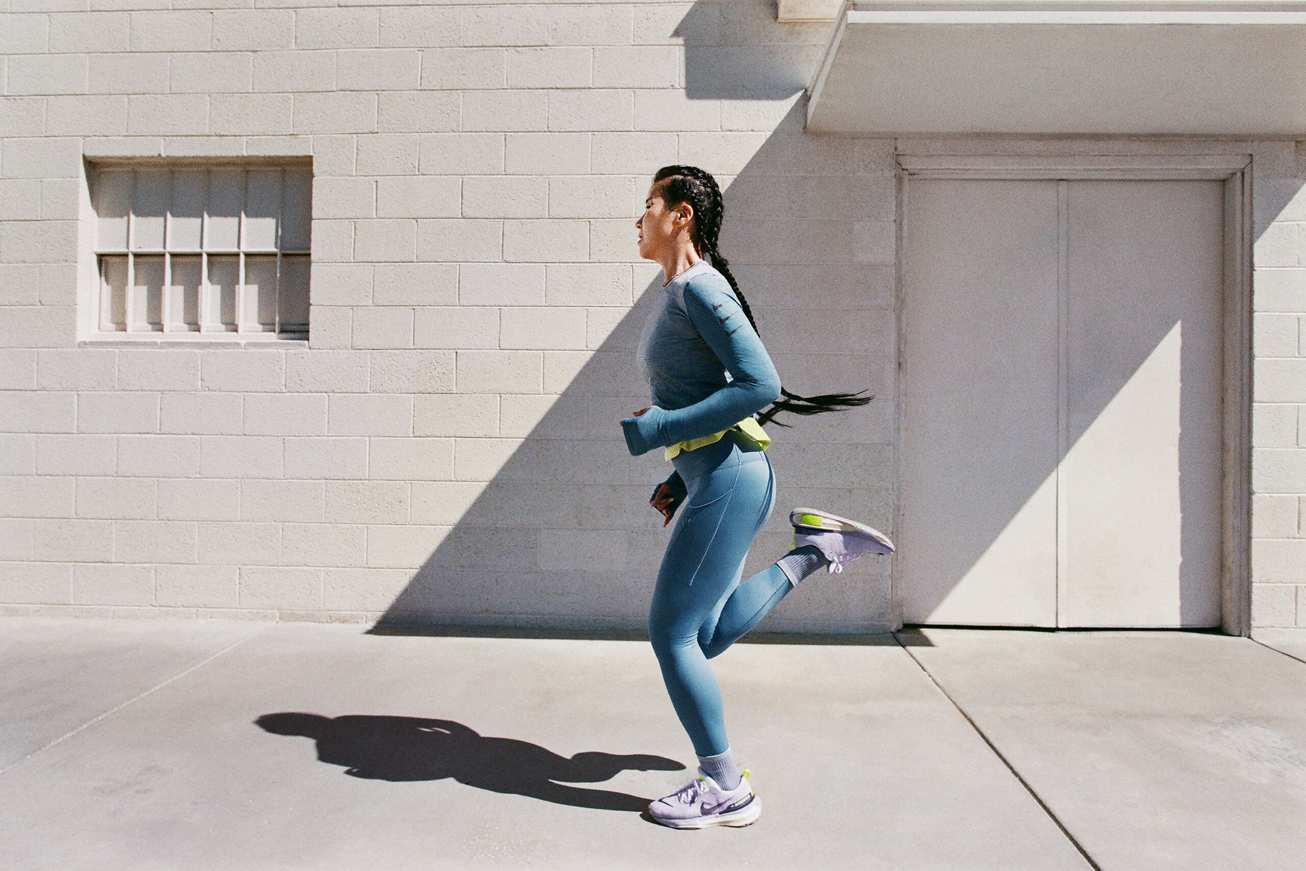 Mi Jang running in front of white building. She is wearing blue running attire with Nike Invincible 3 sneakers