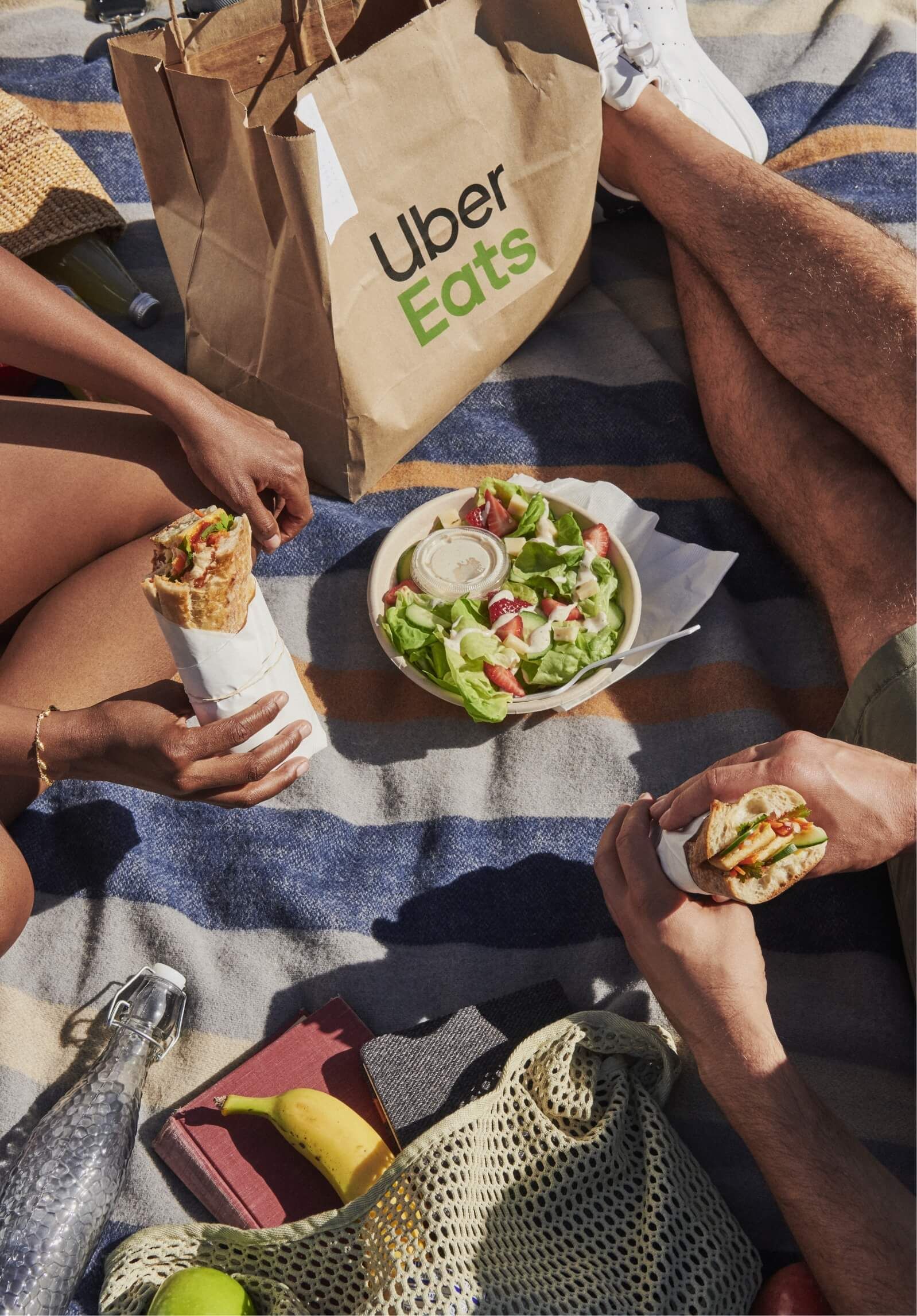 couple on blanket on eating takeout sandwiches and salad from Uber Eats