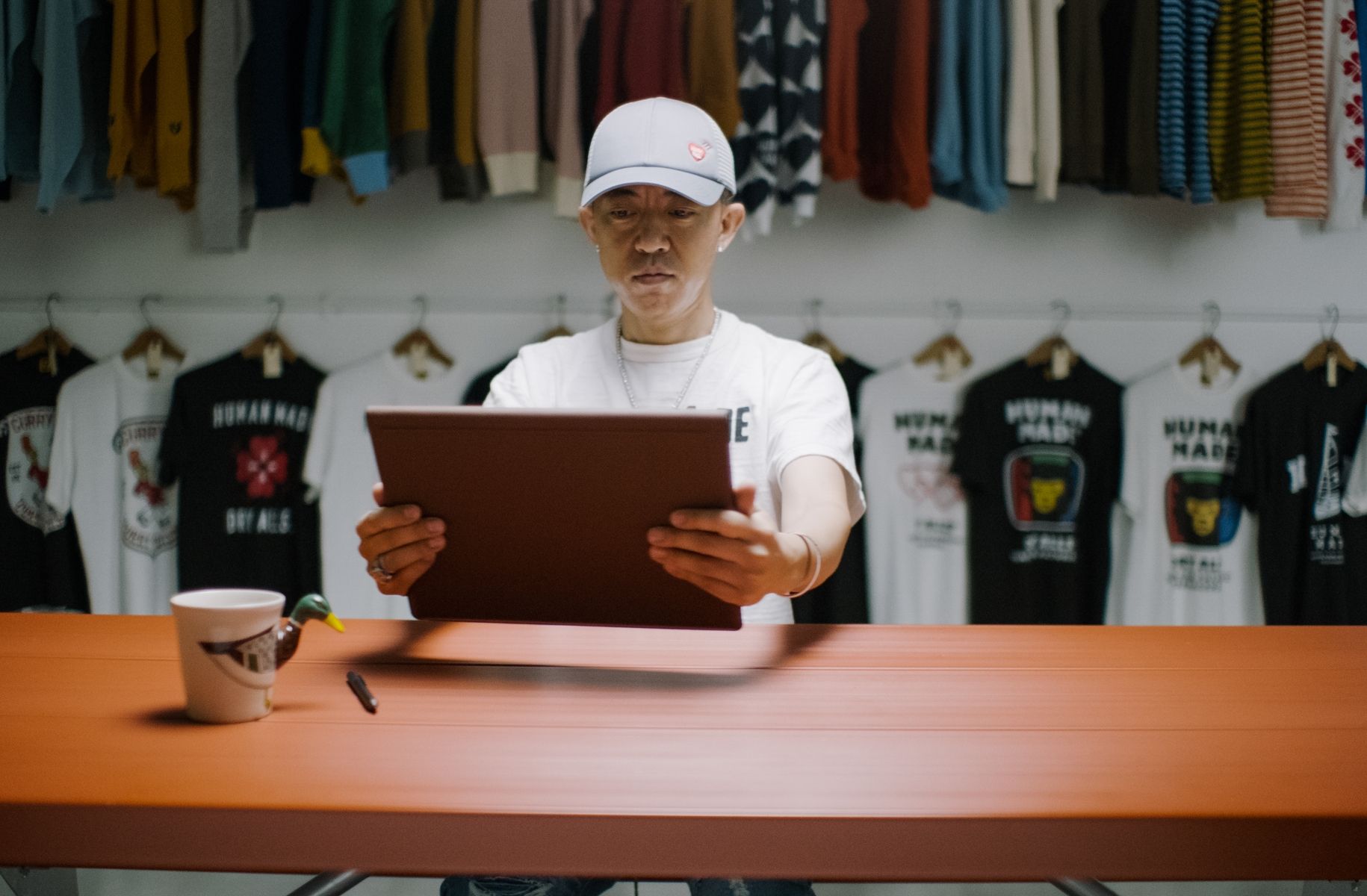 Nigo holding and looking at HP computer in front of his Human Made brand t-shirts