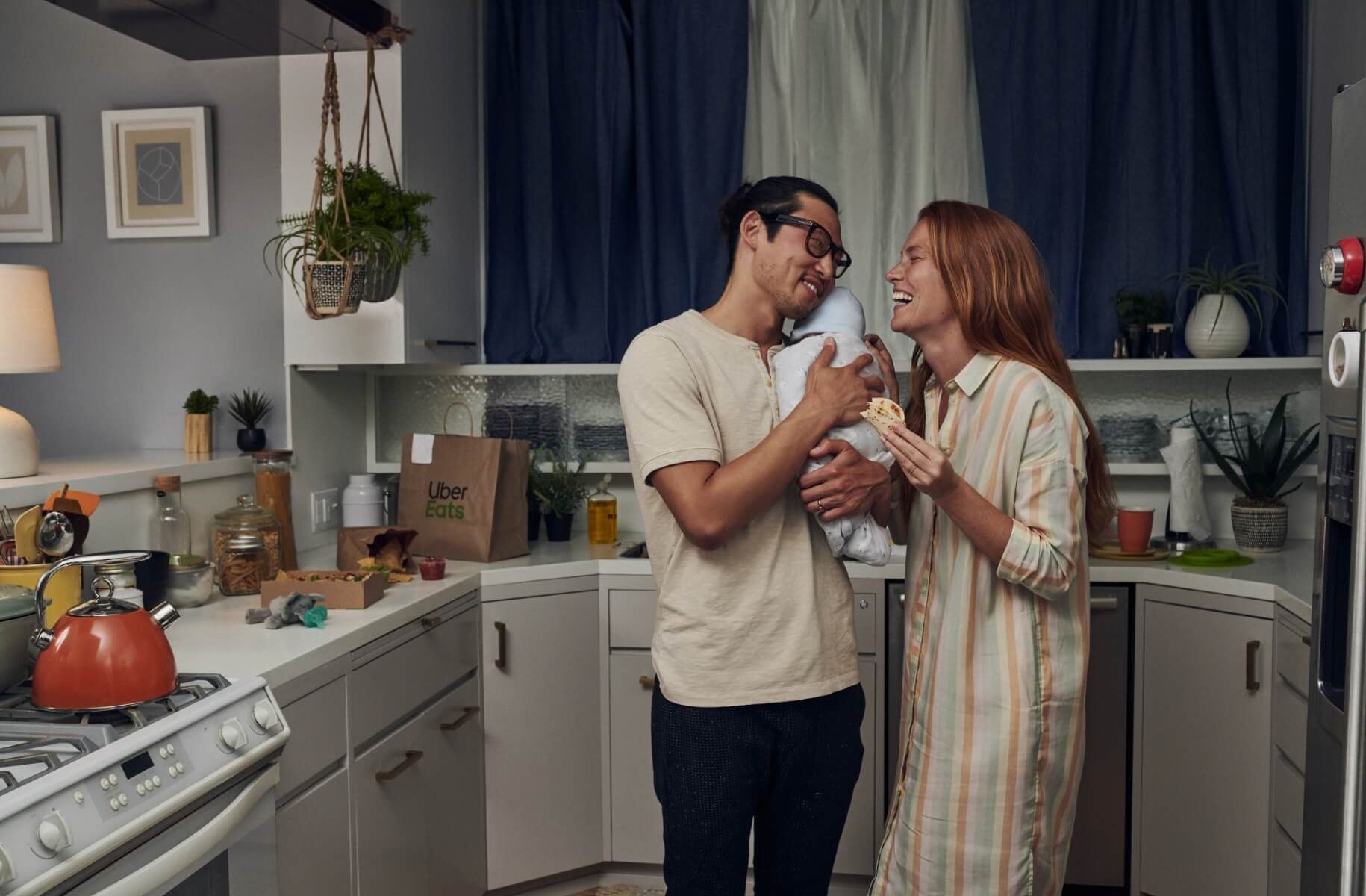 Couple smiling and eat uber eats in kitchen while holding baby at night