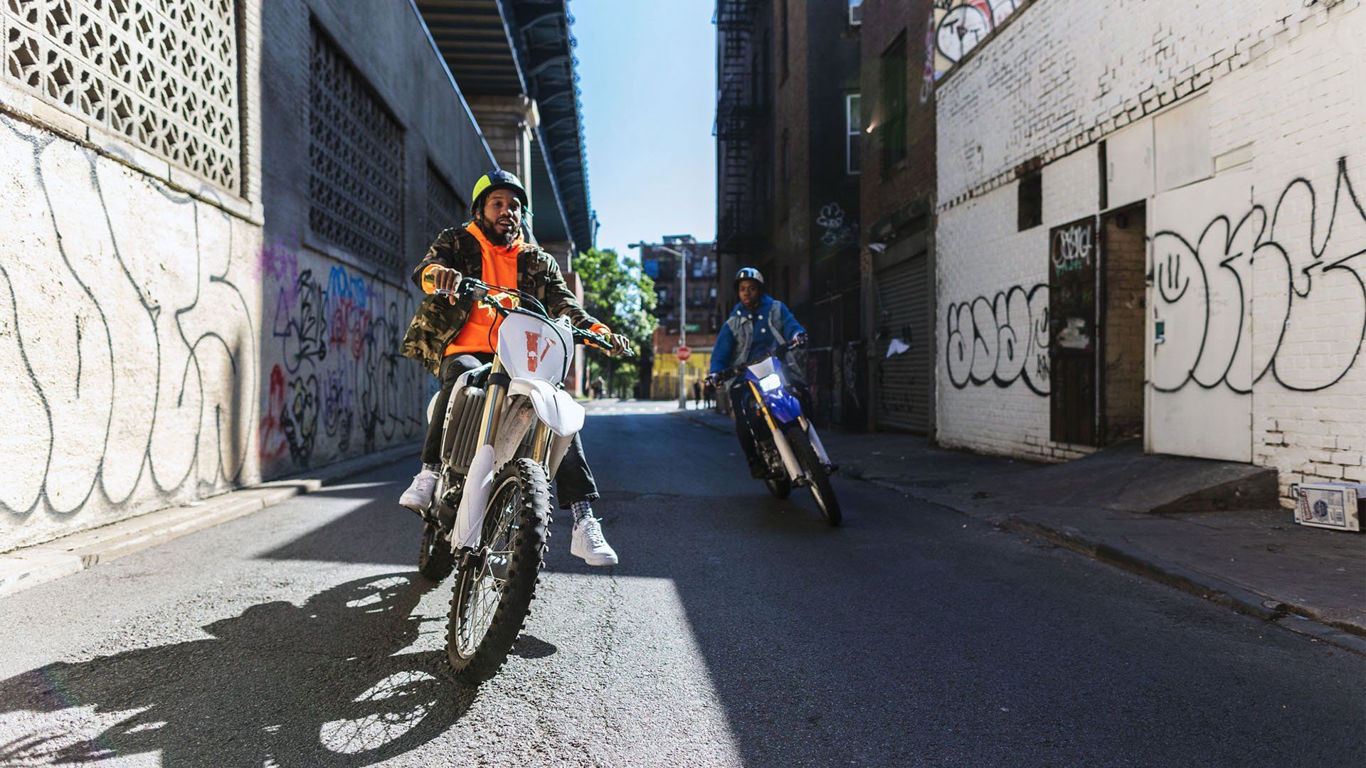 Two men on dirt bikes in city alley