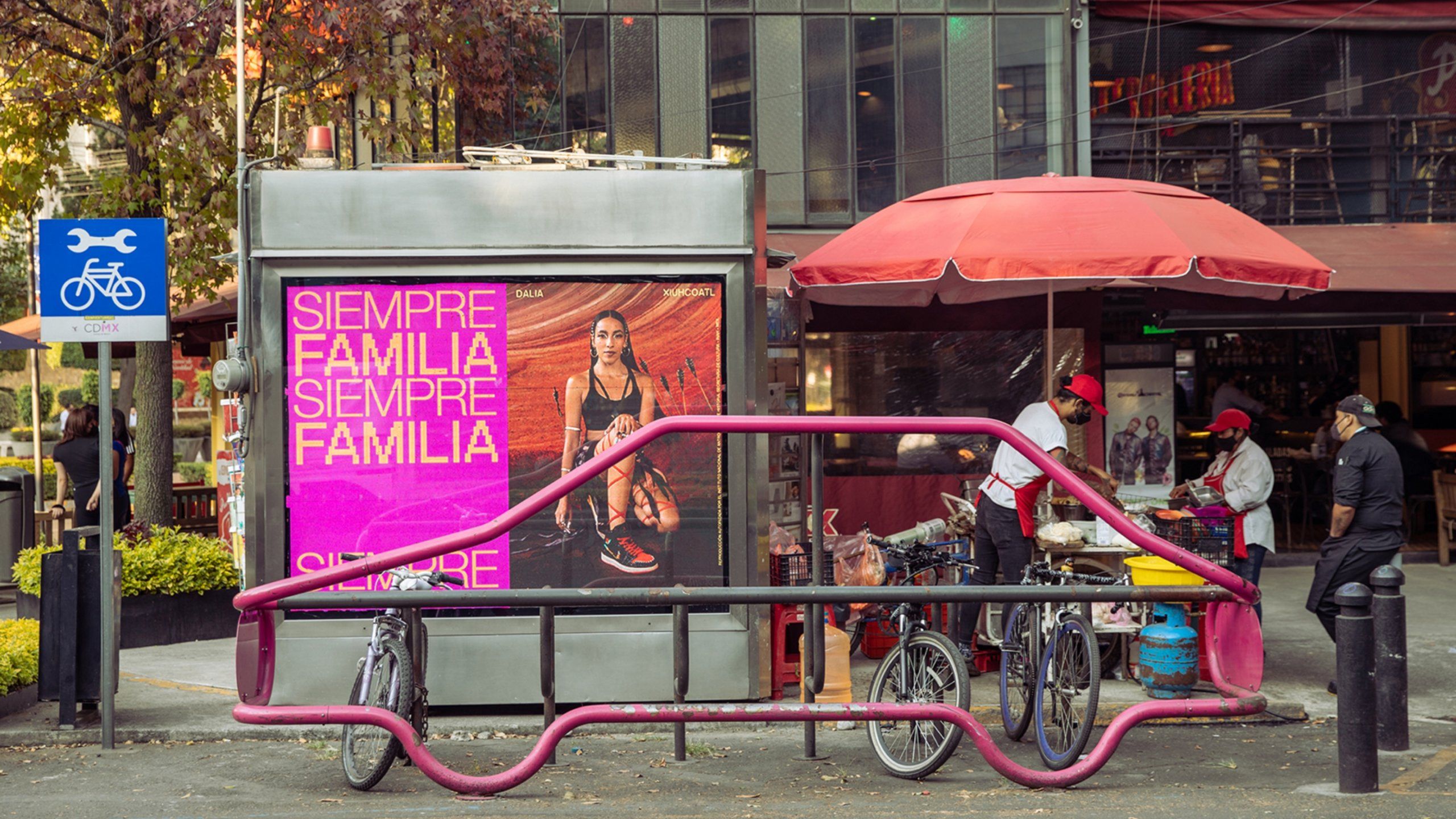 Siempre Familia print ad featuring woman kneeling with arrows embedded into ground behind her at bike locking station in Mexico City