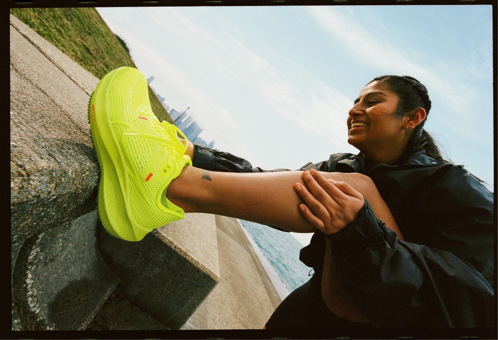 Woman runner smiling with foot up on concrete bench. Her Bright yellow green Nike pegasus 40 is prominent