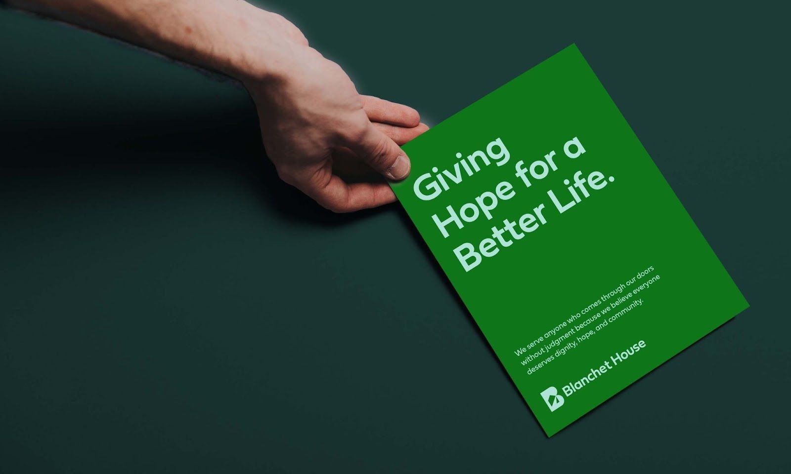 Hand holding booklet reading Giving Hope for a better life. We serve anyone who comes through our doors without judgement because we believe everyone deserves dignity, hope and community.