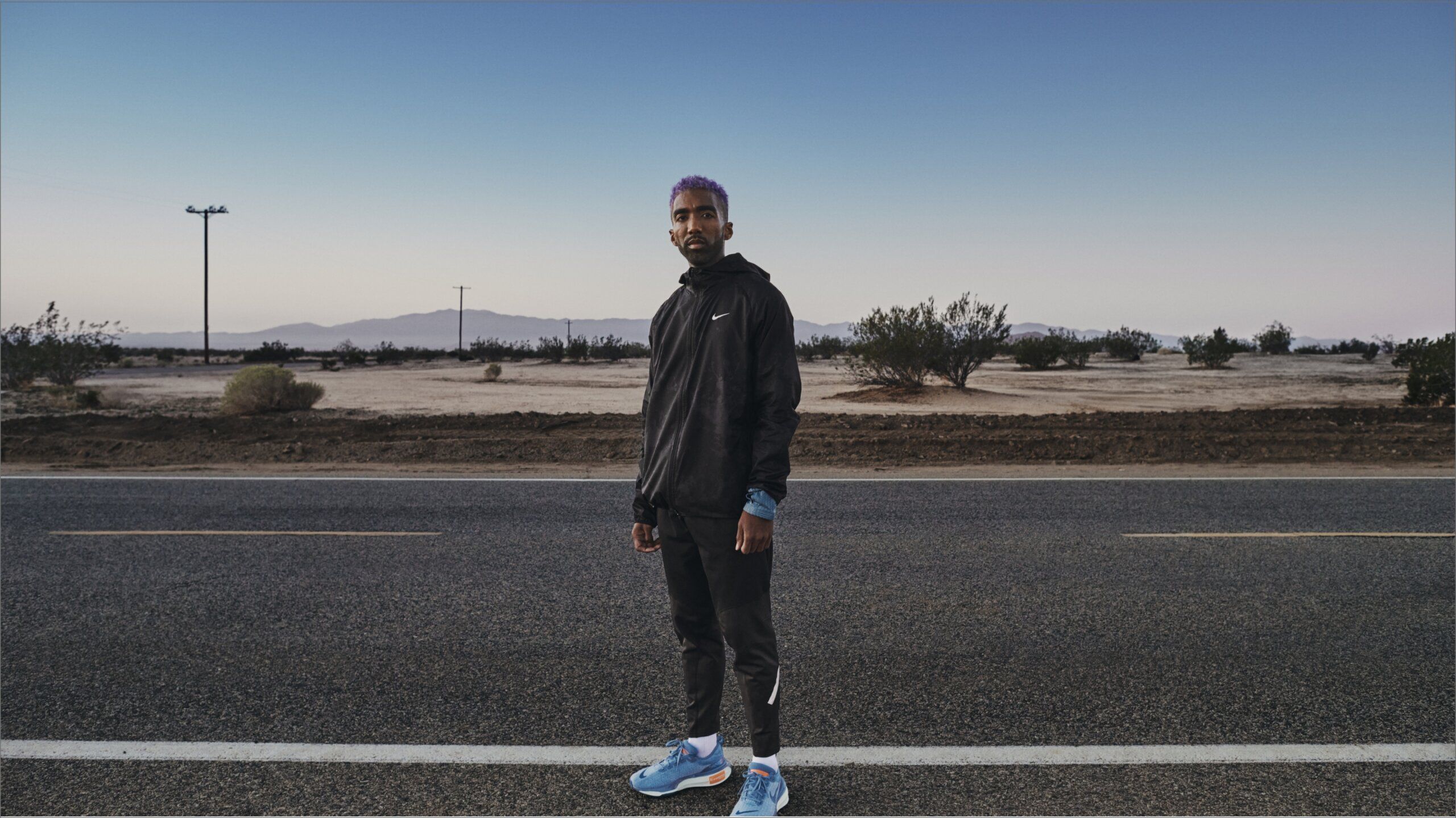 Runner wearing jacket and blue Nike Invincible 3 sneakers on empty road with desert and blue sky behind him