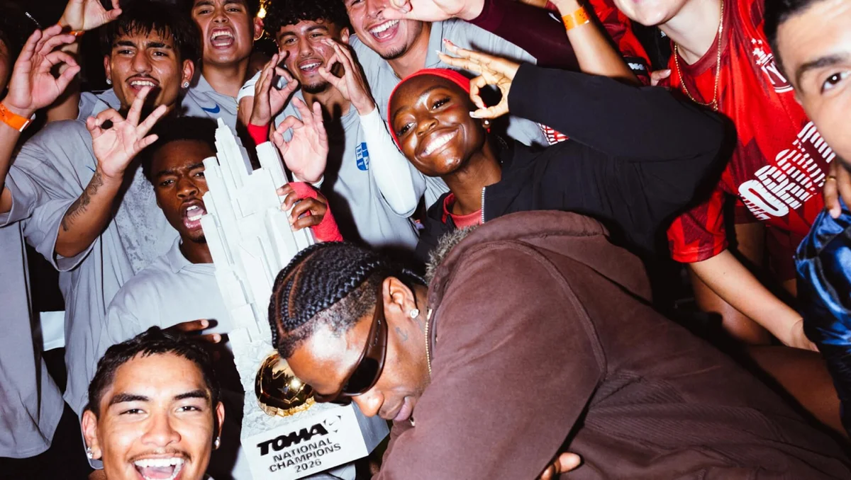 A group of young people poses with a large trophy, smiling and making hand gestures. One person wears sunglasses in the foreground.