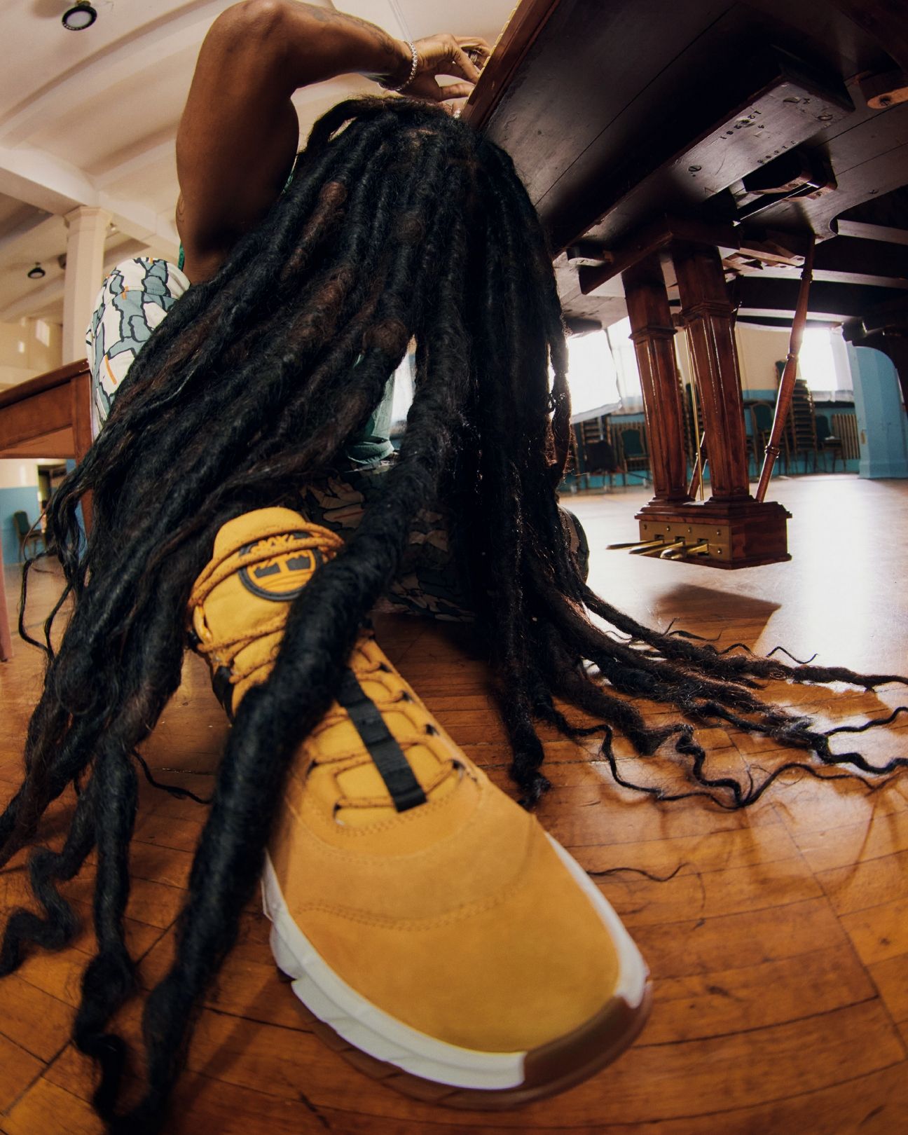 Person with long dreadlocks and timberland shoes at piano with head down so hair goes over shoes